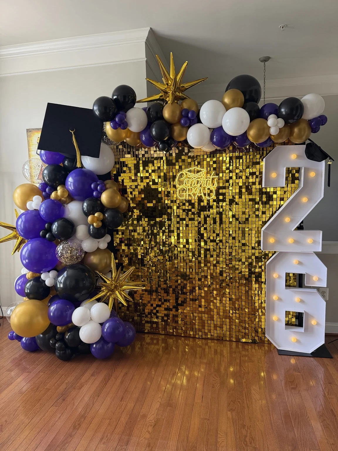 Purple, black, white and gold graduation balloon display with gold shimmer wall and illuminated 26 numbers