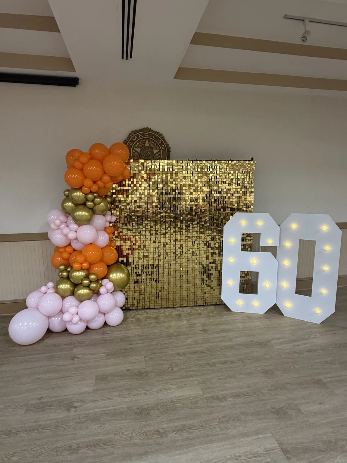 Gold shimmer wall with orange, blush pink and gold balloons beside illuminated 60 numbers