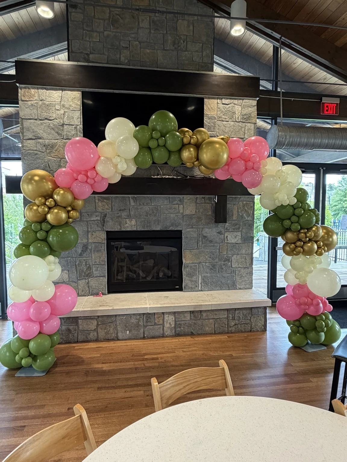 Large organic balloon arch in green, pink, white and gold surrounding a stone fireplace